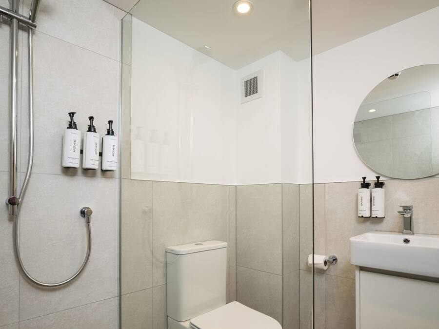 Un baño moderno con ducha de vidrio, inodoro y lavamanos con espejo.