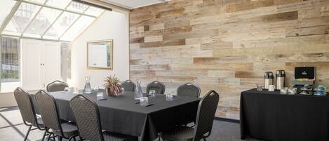A conference room with a long table, chairs, a coffee station, and a large window.