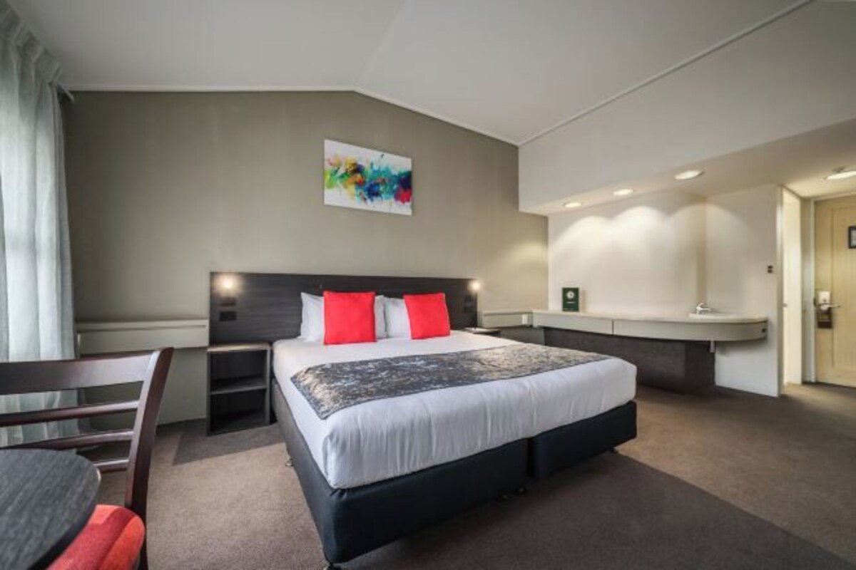 Ein Hotelzimmer mit einem großen Bett, einem Schreibtisch, einem Sessel und einem Bild an der Wand.