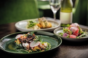 Trois assiettes de nourriture sont disposées sur une table, avec une bouteille de vin et un verre de vin en arrière-plan.