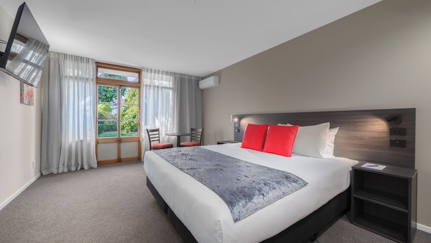 A hotel room with a large bed, a desk, a chair, and a view of the outdoors. -  Carnmore Hotel Lower Hutt (Lower Hutt)