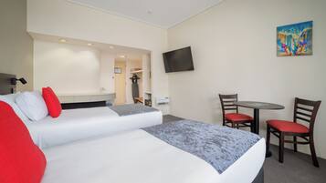 A hotel room with a large bed, two chairs, a small table, a TV, and a painting on the wall.