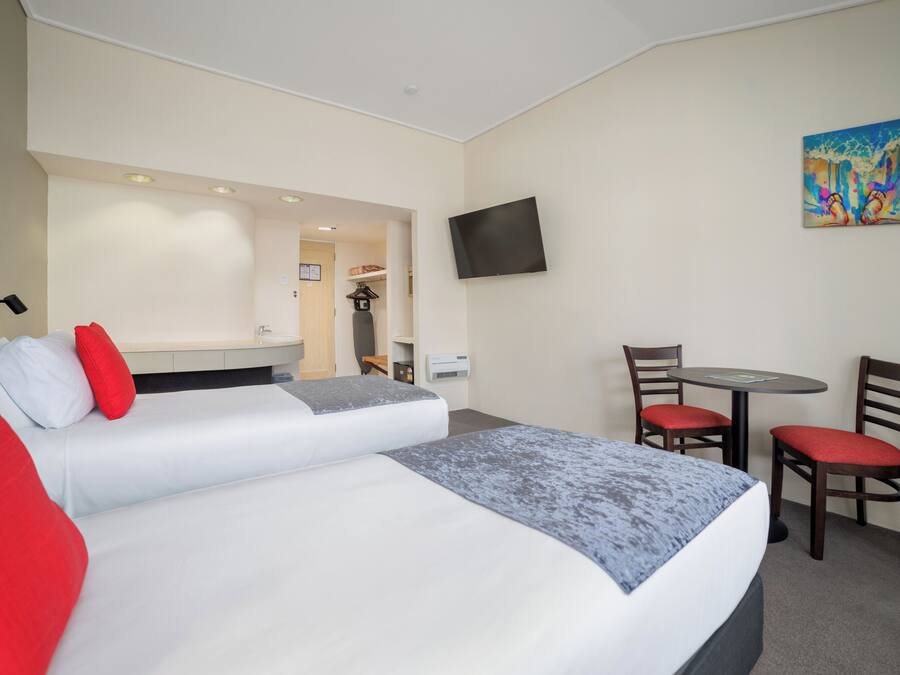 A hotel room with a large bed, two chairs, a small table, a TV, and a painting on the wall.