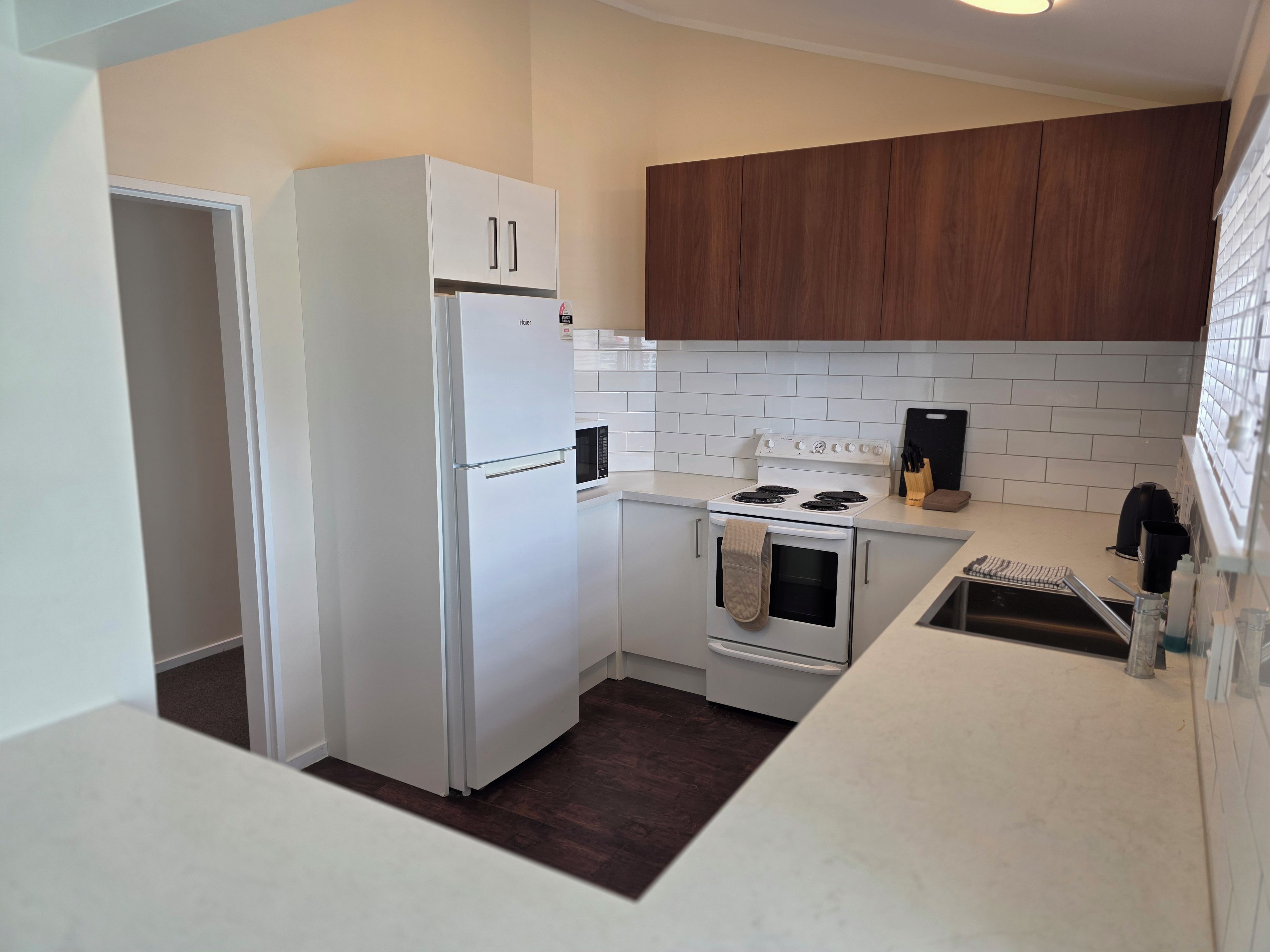 Una cocina compacta con muebles blancos, horno empotrado, estufa y microondas.