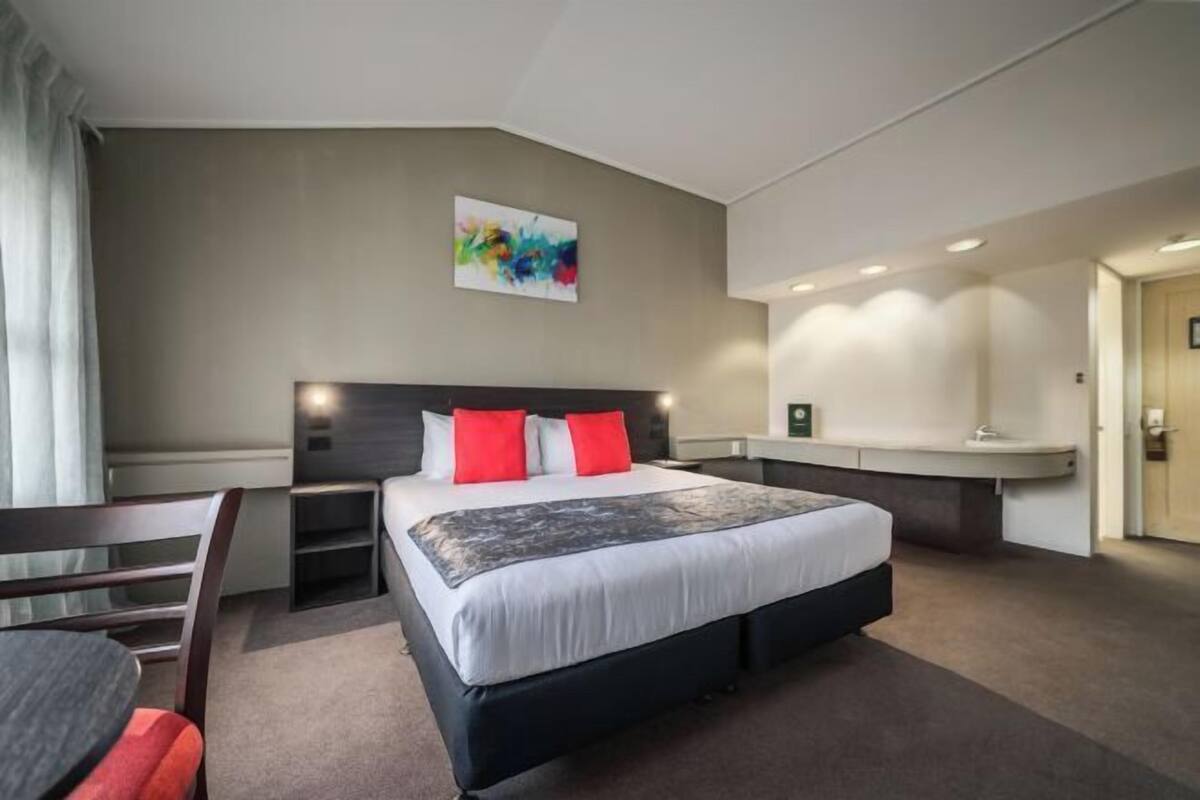 Quarto de hotel com uma cama grande, uma escrivaninha, uma cadeira e um quadro na parede.