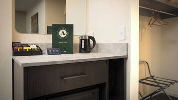Habitación de hotel con kitchenette, cafetera, espejo y perchero.