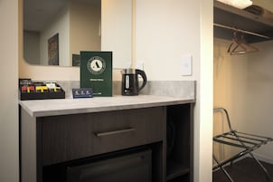 Habitación de hotel con kitchenette, cafetera, espejo y perchero.