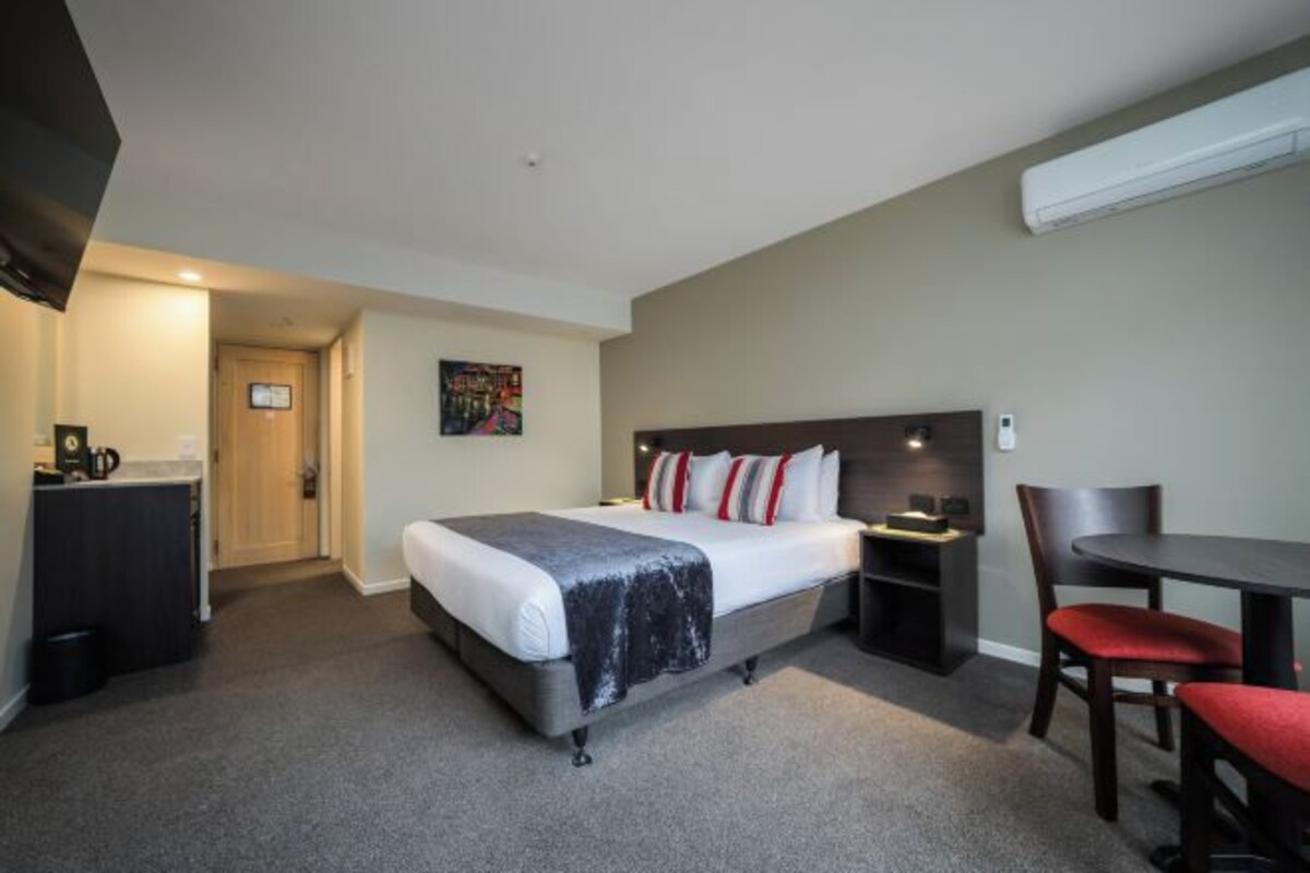 Ein Hotelzimmer mit Bett, Nachttisch, Stuhl und Schreibtisch mit Sitzmöglichkeit.