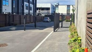 Ein durch einen Zaun gesicherter Parkbereich mit einem modernen Gebäude im Hintergrund.