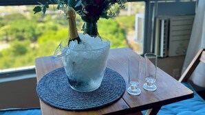 Ein Tisch mit Blumen in einer Vase, einer Champagnerflasche und zwei Gläsern auf einer Matte, mit Blick auf eine reizvolle Aussicht.