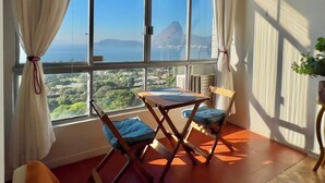 Ein Zimmer mit großem Fenster, einem Tisch, zwei Stühlen und einem Blumentopf.