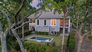 Une maison à deux étages avec une piscine, entourée d’arbres et d’une cour clôturée.