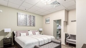 Habitación de hotel moderna con una cama grande, un rincón de descanso y un baño visible a través de una puerta abierta.