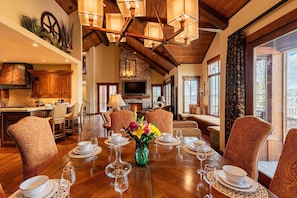 A dining room with a wooden table set for six, surrounded by patterned chairs, a fireplace, and a television.