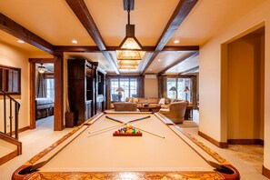 A pool table in a room with wooden beams, a chandelier, and a seating area with a view.