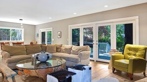 A modern living room with a sofa, armchairs, a glass coffee table, and a dining area with chairs.
