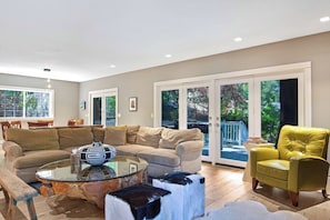 A modern living room with a sofa, armchairs, a glass coffee table, and a dining area with chairs.