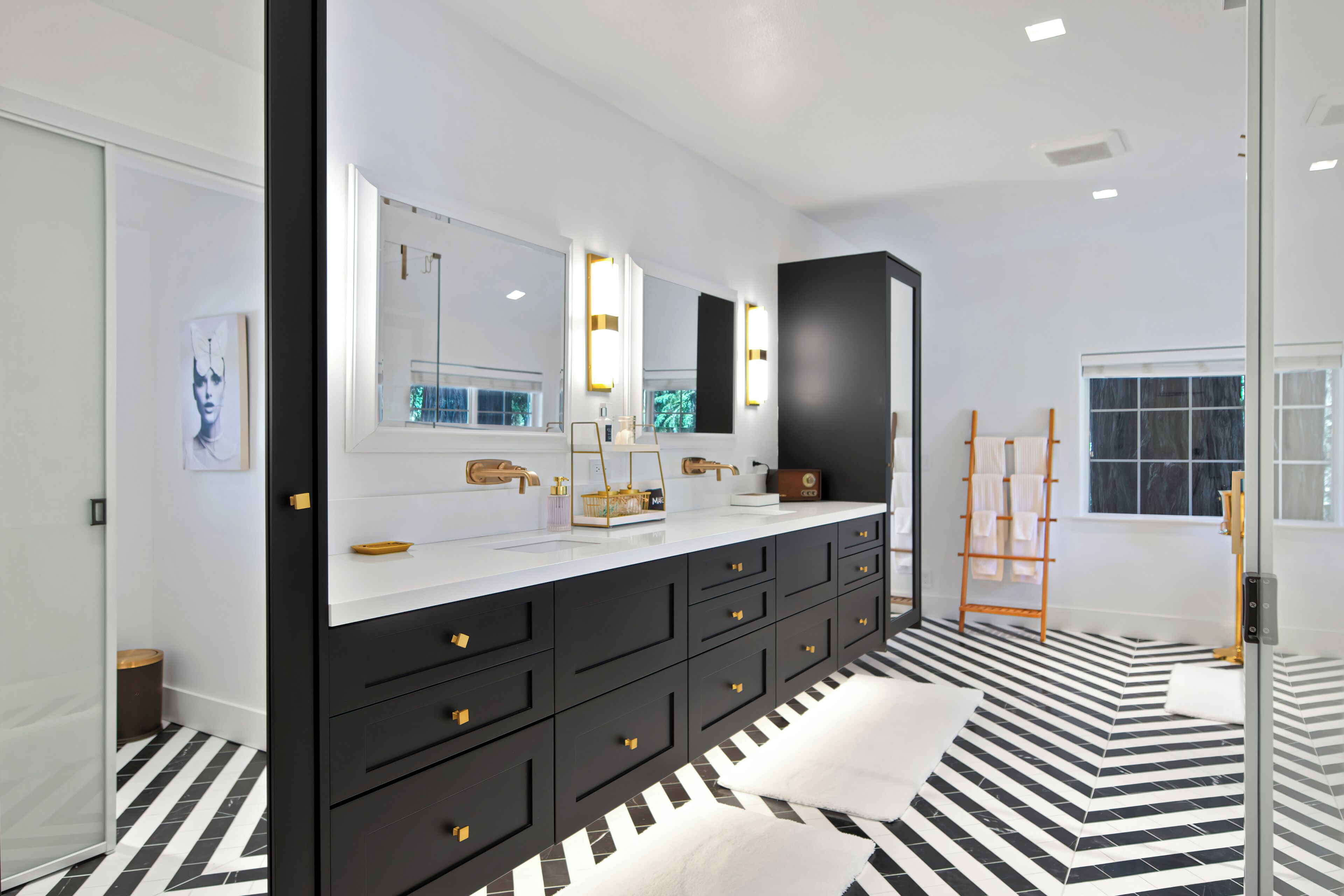 Une salle de bain moderne avec un grand miroir, un carrelage noir et blanc à motifs et un meuble noir.