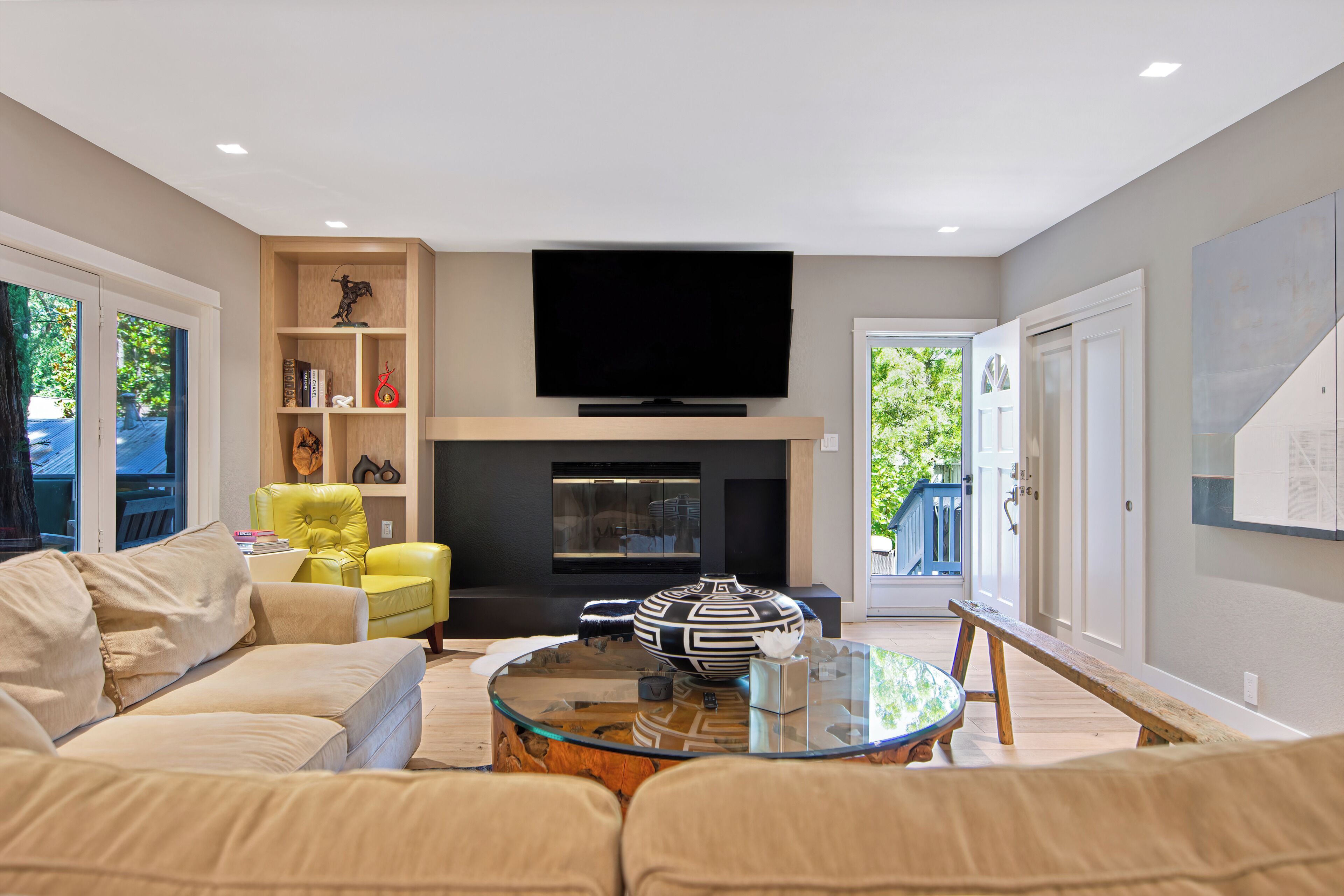 A living room with a sofa, a yellow chair, a fireplace, a flat-screen TV, and a glass coffee table.