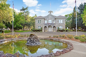 A stone building with a clock tower, a flagpole, and a fountain in front.