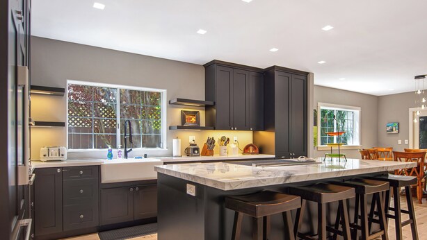 A modern kitchen with dark cabinets, a large island with bar stools, and a window with a view of trees.