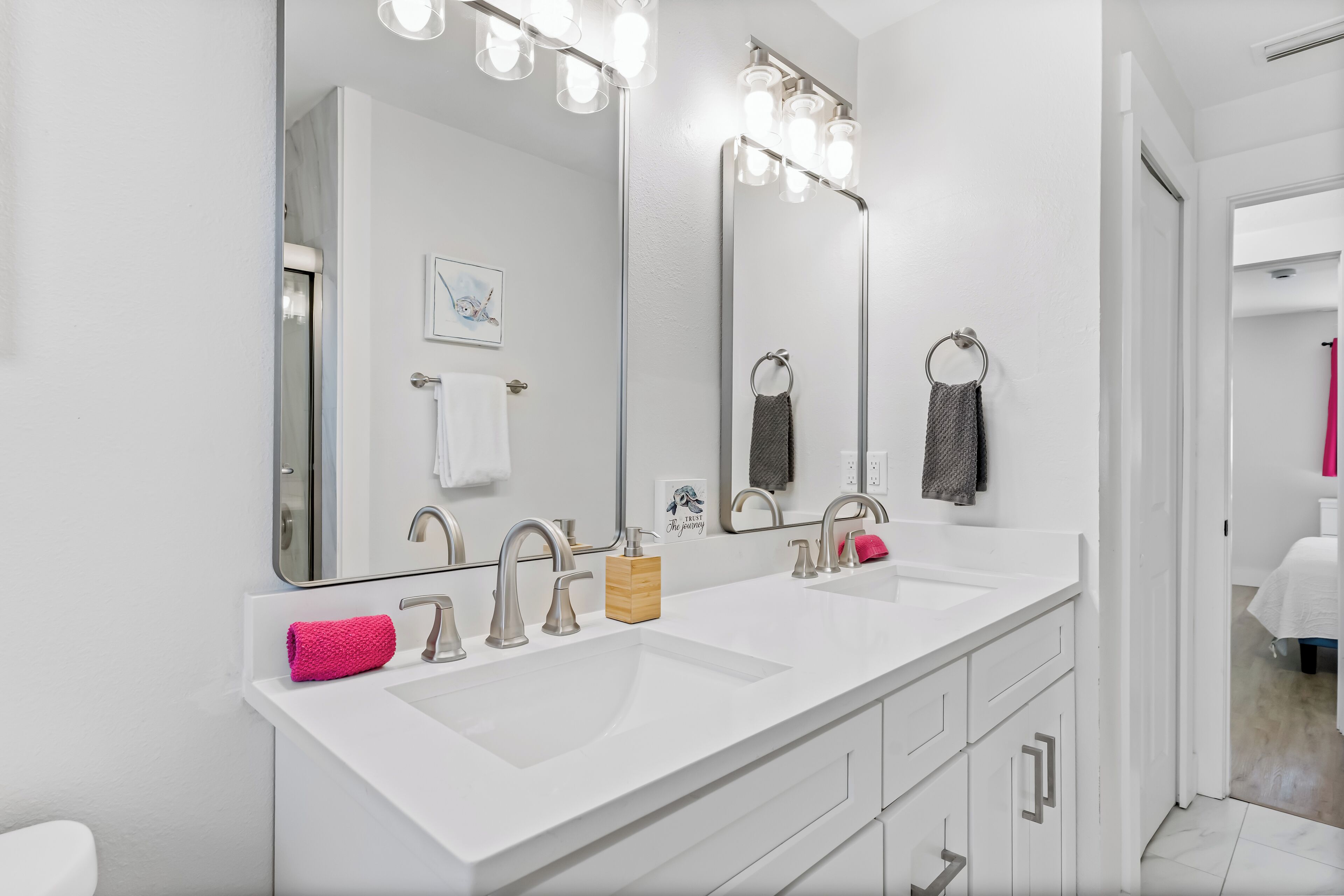 Une salle de bain moderne avec un meuble-lavabo blanc, deux vasques et un grand miroir avec éclairage intégré.