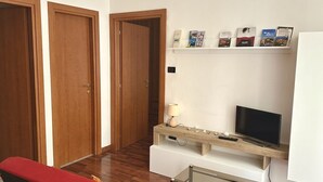 A room with a TV, a shelf with books, a bench, and two wooden doors. - A38 - Ancona, comfortable two-room apartment in the historic center (Ancona)