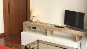A room with a wooden TV stand, a television, a lamp, and a glass table. - A38 - Ancona, comfortable two-room apartment in the historic center (Ancona)