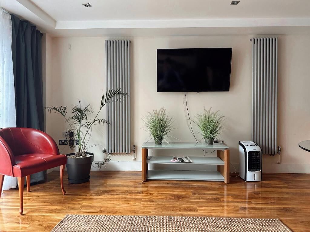 Un salon moderne avec un fauteuil rouge, une table basse en verre, deux plantes en pot, un téléviseur à écran plat et un radiateur portatif.