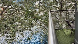 A view of a rooftop garden with a small pond, surrounded by trees and a metal railing. - Canary Wharf Apartments (London)