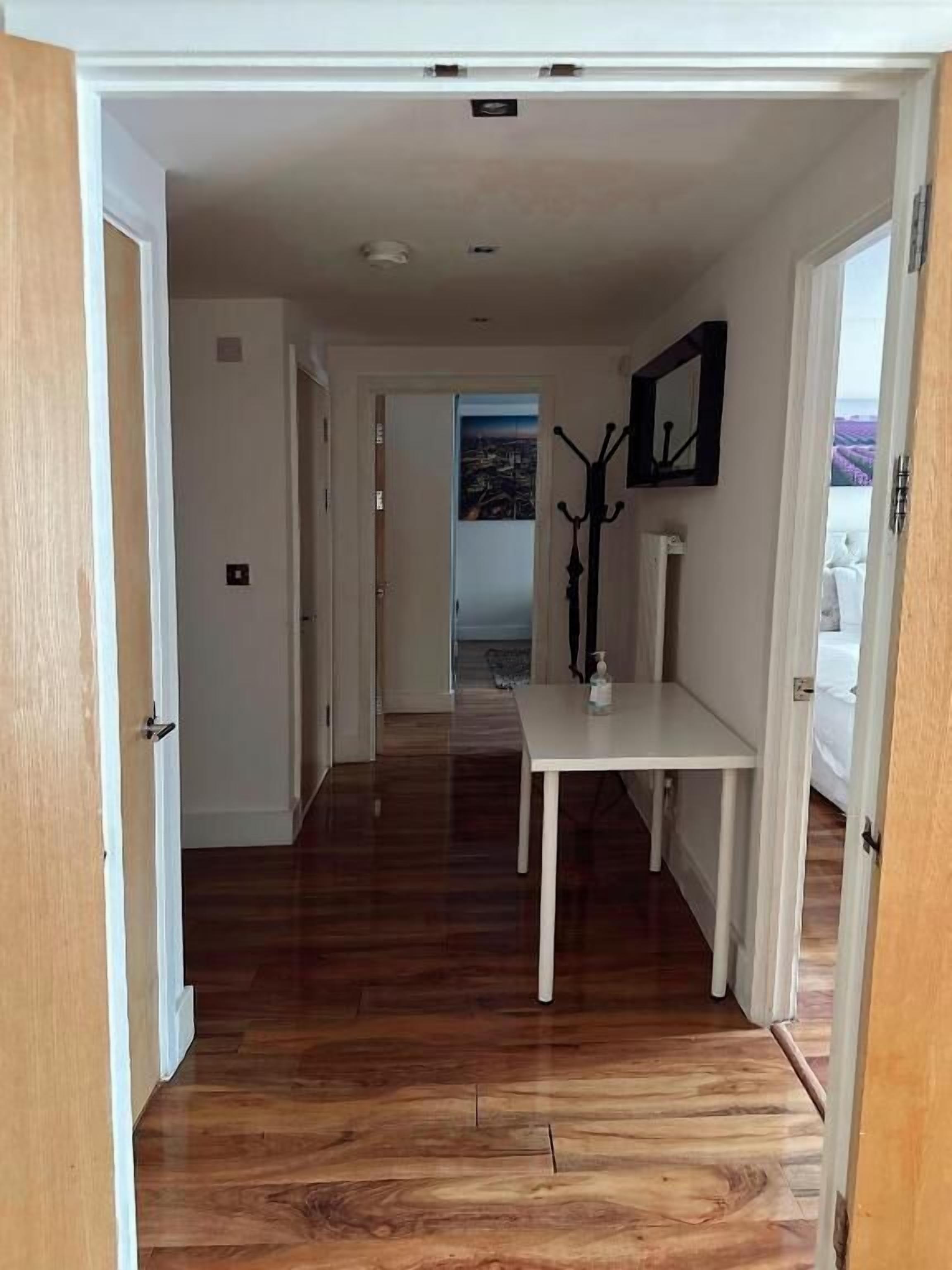 A hallway with wooden flooring leading to a room with a white table and a coat rack.