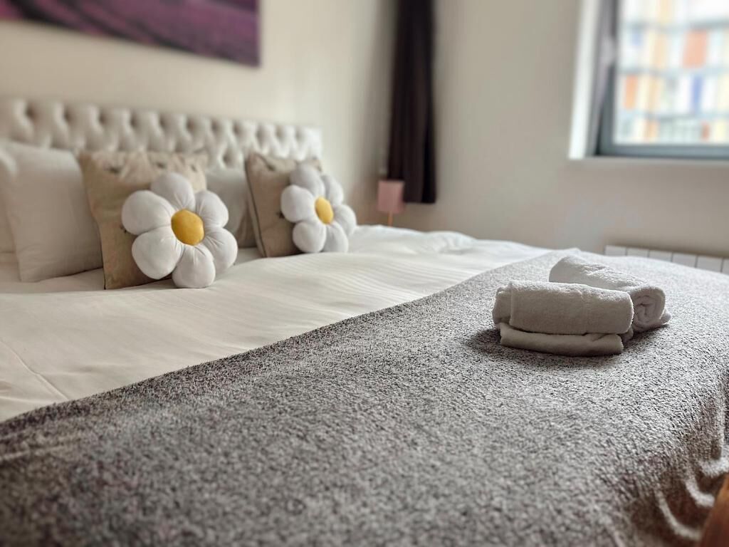 A neatly made bed with a grey textured blanket and two white pillows with yellow centers.