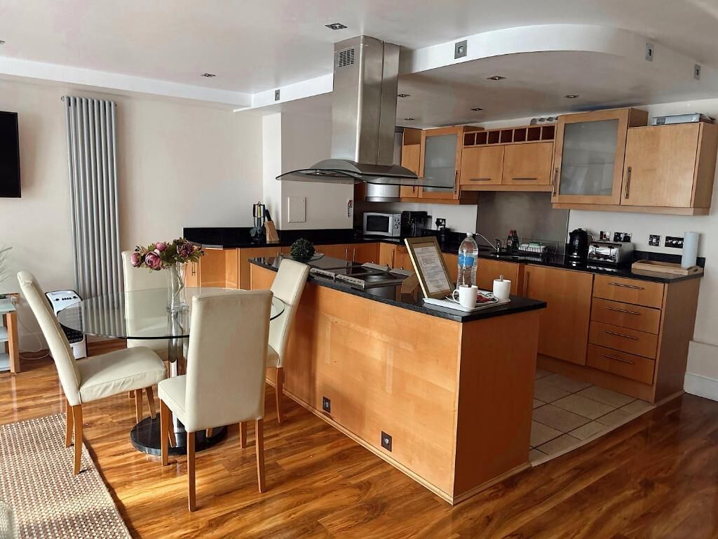 A modern kitchen with wooden cabinets, a central island, and a dining area with a glass table and chairs.