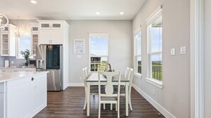 Una cocina moderna con armarios blancos, un refrigerador de acero inoxidable y un comedor con mesa y sillas blancas.