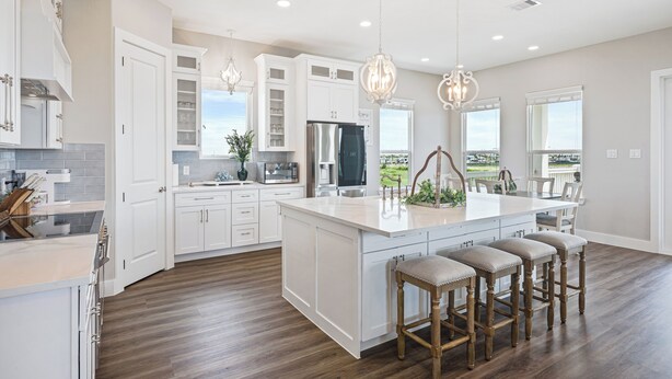 Una cocina amplia con armarios blancos, una isla grande con taburetes de bar e iluminación colgante.