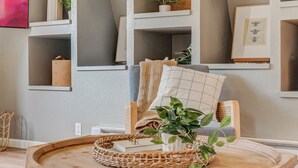 Ein gemütliches Wohnzimmer mit einem runden Holztisch, einem bequemen Sessel und einem Bücherregal voller Bücher und Dekoration.