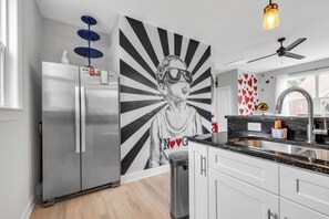 Une cuisine moderne dotée d’un réfrigérateur en acier inoxydable, d’une fresque murale et d’un ventilateur de plafond.