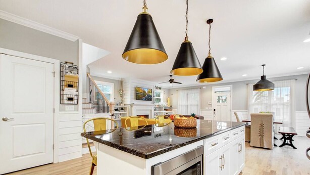 Une cuisine moderne dotée d’un îlot central, de meubles blancs et de luminaires suspendus noirs.