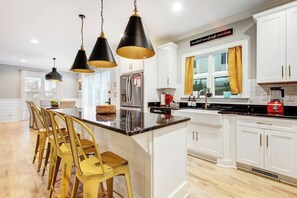 Una cocina moderna con armarios blancos, una isla central y un comedor con sillas amarillas.