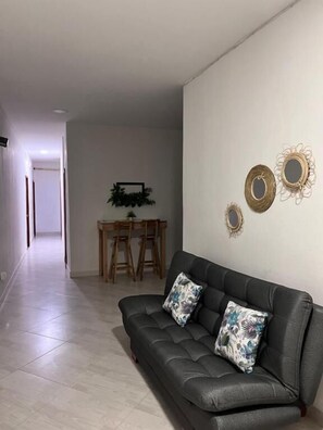 Una sala moderna con un sofá gris, dos espejos decorativos y un comedor con una mesa y sillas de madera.