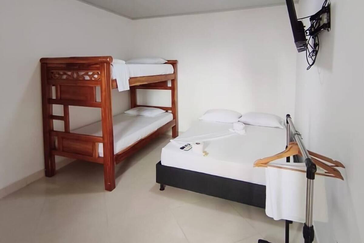 Una habitación con dos camas literas de madera, una mesa pequeña con mantel blanco y un televisor instalado en la pared.