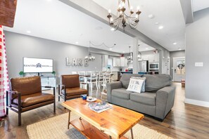 A modern living room with a grey sofa, brown leather chairs, a wooden coffee table with magazines, and a chandelier.