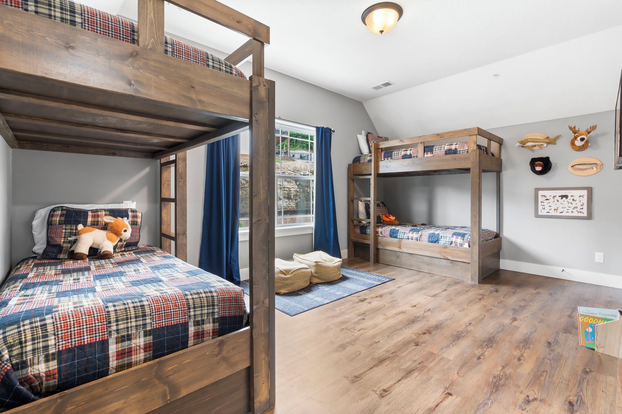 Una habitación con literas, una ventana con cortinas, una alfombra y adornos de animales en la pared.