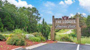 Et træskilt med 'The Lodges Chateau Cove' skrevet på, omgivet af vegetation og en belagt indgang.