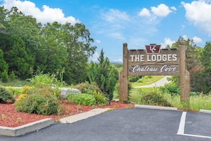 A wooden sign with 'The Lodges Chateau Cove' written on it, surrounded by greenery and a paved entrance.