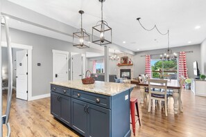 A modern kitchen with a central island, wooden flooring, and pendant lighting.