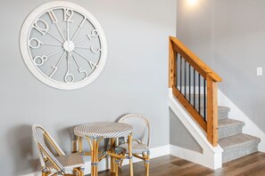 Una escalera con escalones de madera y barandilla, un reloj de pared y una mesa con dos sillas.