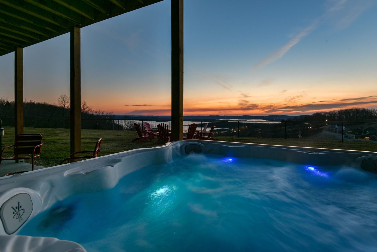 A hot tub with a view of a sunset over a body of water, surrounded by chairs and a covered area.