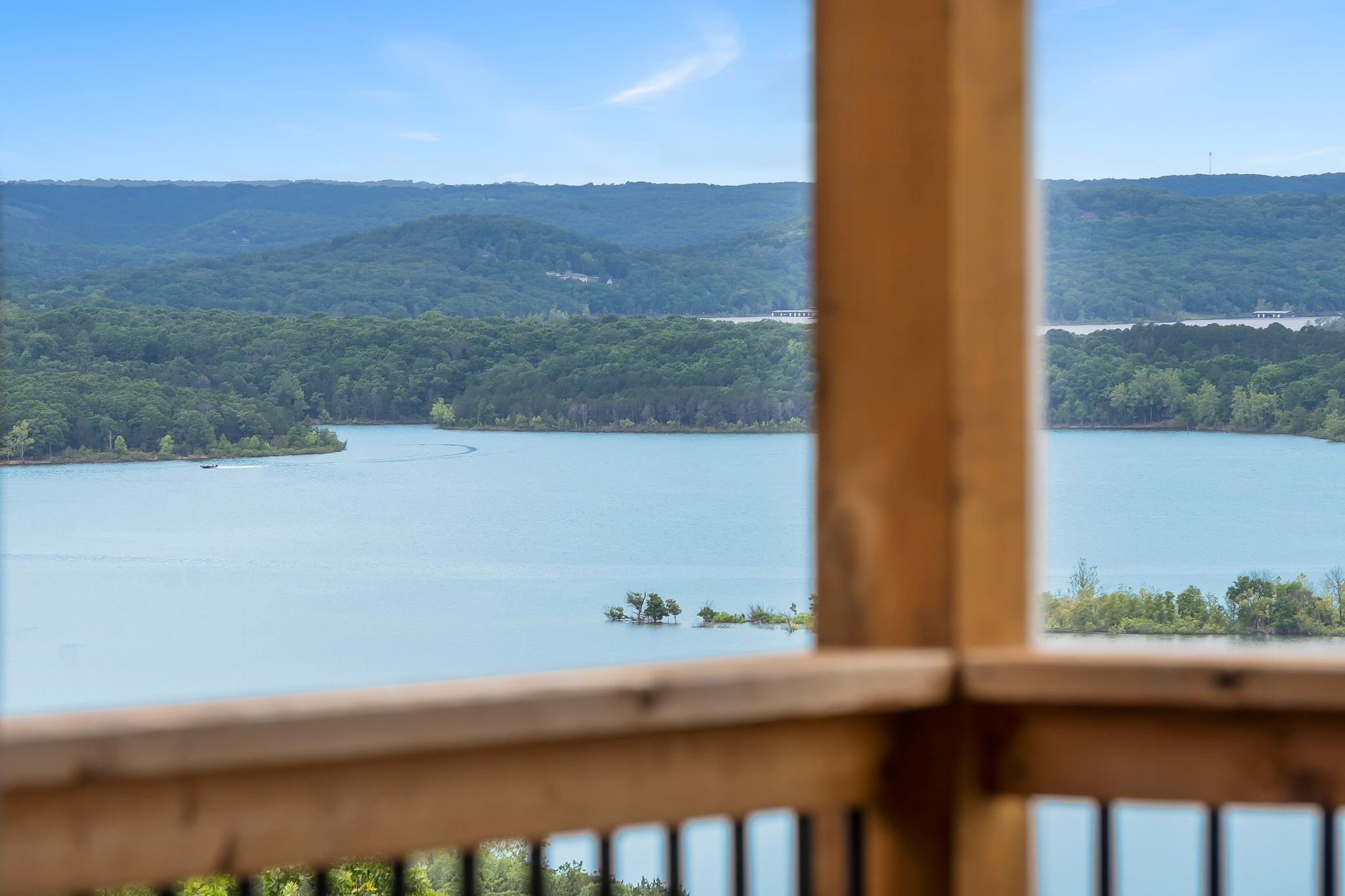 Blick auf einen See von einer Holzterrasse bei blauem Himmel.