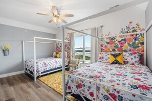Un dormitorio con dos camas, ventilador de techo, vistas al exterior y un cabecero estampado con motivos florales.